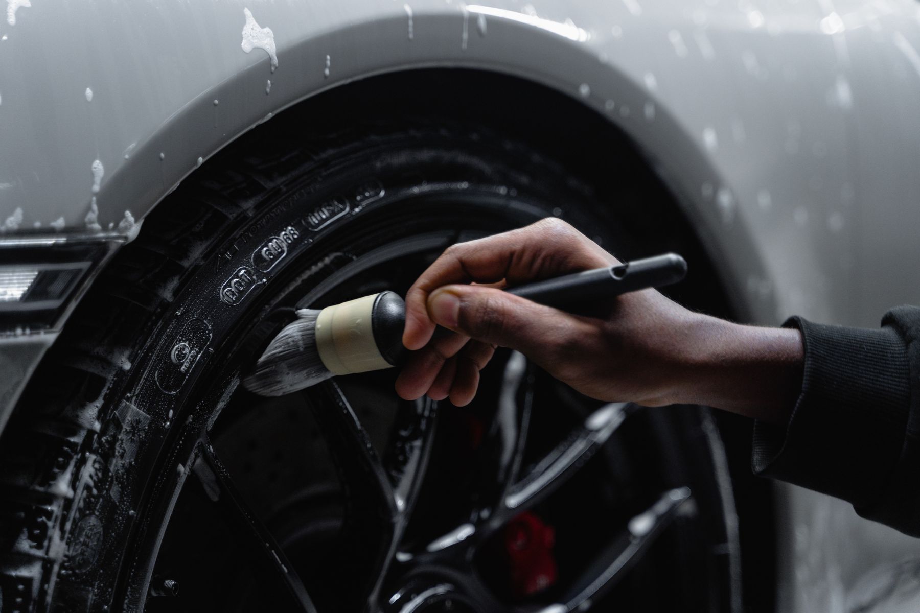 A wheel being carefully cleaned with a detailing brush